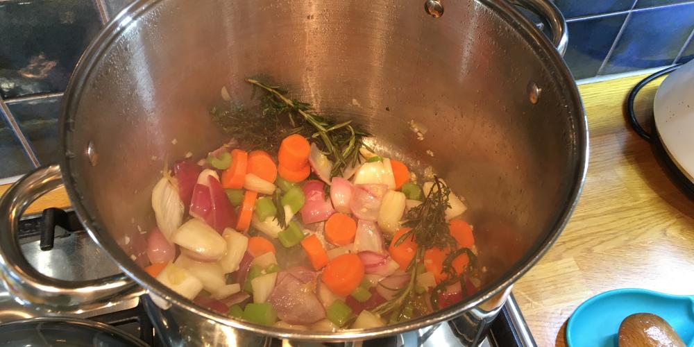 A pot on the hob steams with chopped vegetables and herbs.