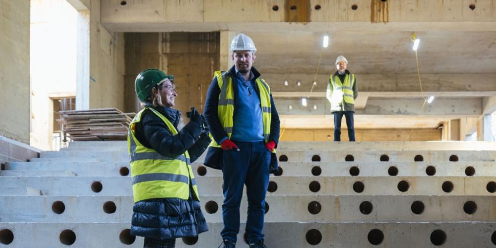 Trinity College president Hilary Boulding stands talking to a member of staff in the auditorium basement of the Levine Building. They are wearing hard hats and hi-vis jackets.