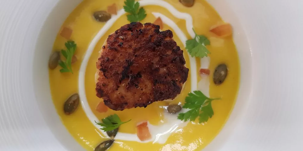 A bowl of butternut squash soup with seared scallop and pumpkin seeds.