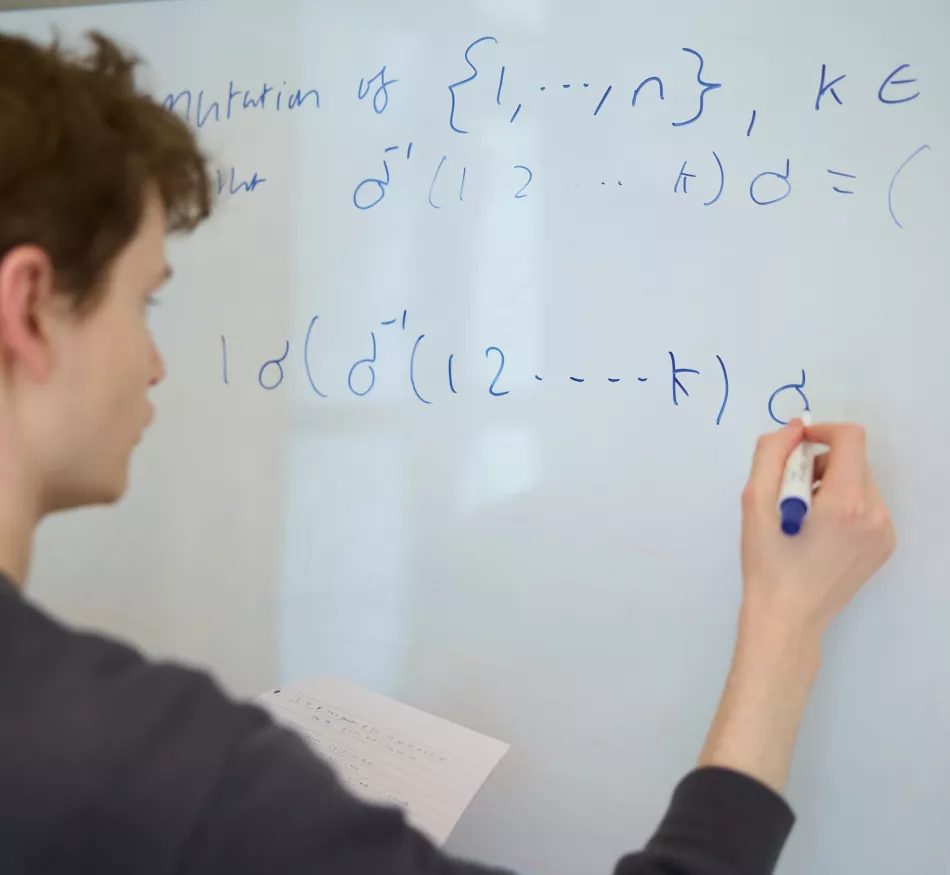 A student writes a maths equation on a whiteboard.