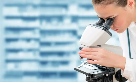 A female student in a lab coat stares down a microscope.