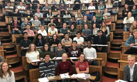 A group of students sit in a lecture theatre listening to an academic lecture.