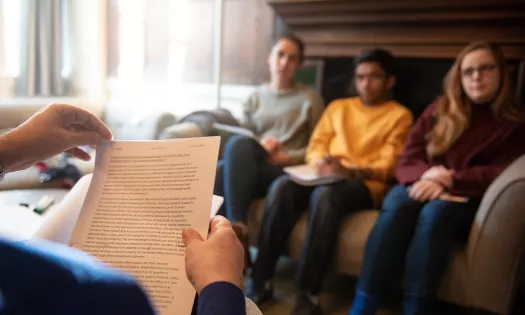 A biomedical sciences tutorial at Trinity - the hands of a tutor reading a paper are the foreground; three students sit on a couch across from him out of focus.