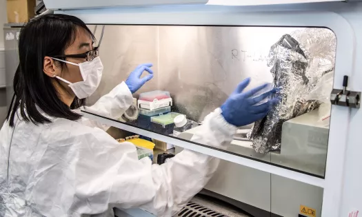 An engineering student in lab coat, goggle and globes performs an experiment.