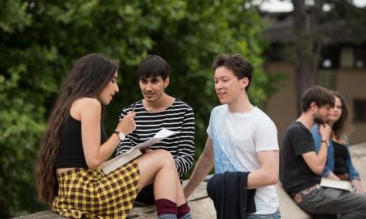 Two male students and one female student sit talking outside the English Faculty.