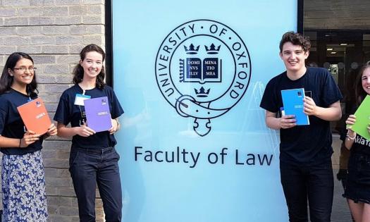 Students pose outside a sign reading 'Faculty of Law' holding undergraduate prospectuses.