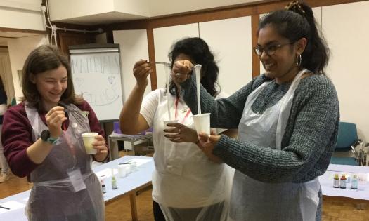 A group of female students stands in aprons doing a materials experiment.