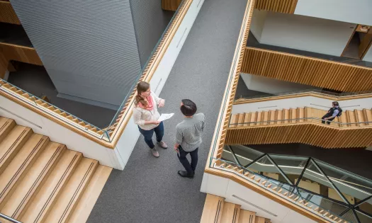 Two students stand talking on a staircase landing in the maths department. The image is taken from above.