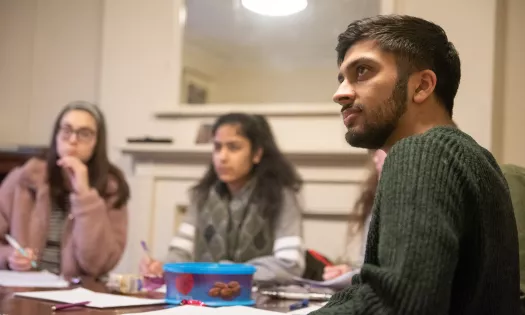 Three students (a male in the foreground and two fem ales in the background) listen during a tutorial.