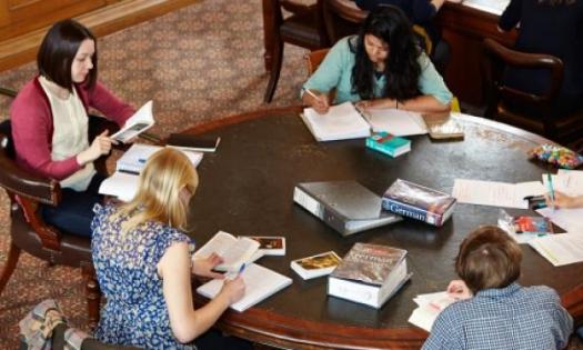 A group of students sit at a table studying; a German dictionary sits on the table in the middle.