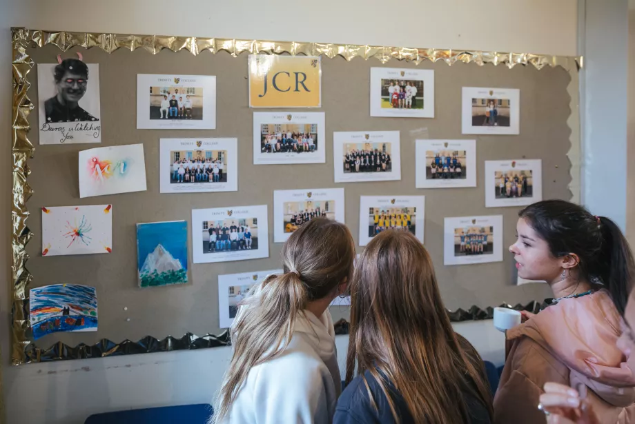 JCR Freshers look at a bulletin board with pictures in the Trinity JCR.