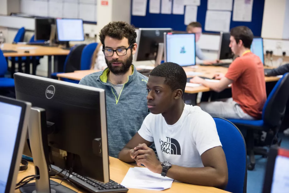 A teacher looks at a computer screen with a student. 