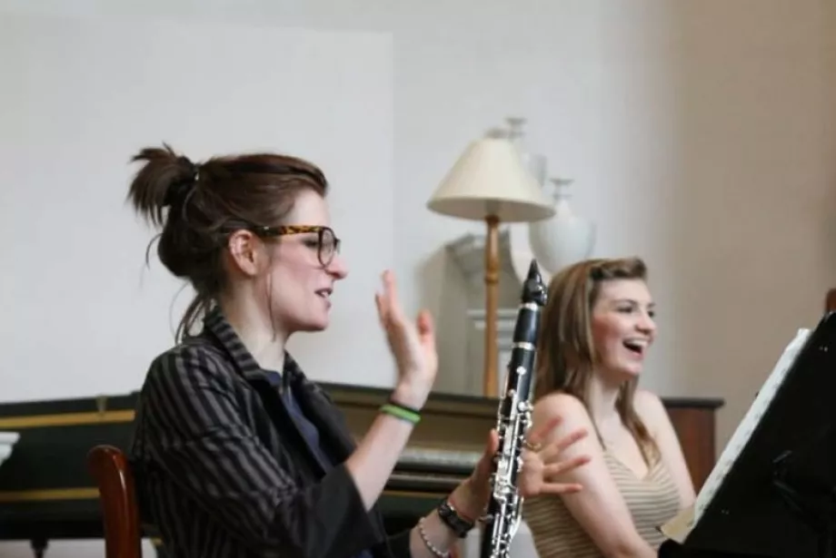 A female student with a clarinet smiles while another student in the background laughs during a music session.