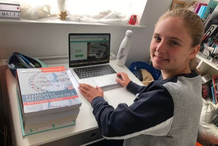 A student sits at her computer studying and is turned smiling at the camera.