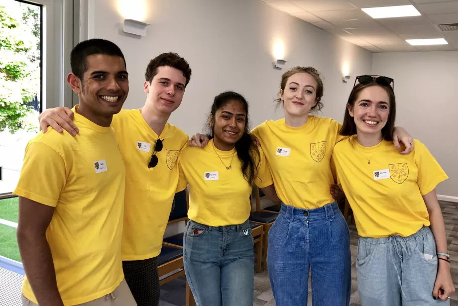 A group of five male and female Trinity students in yellow Open Days t-shirts stand with arms around each other at an Open Day.