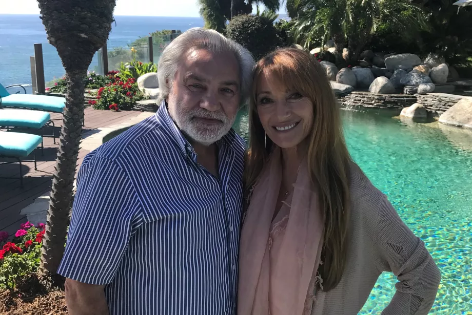 Jane and David stand in front of a pool with flowers and trees around