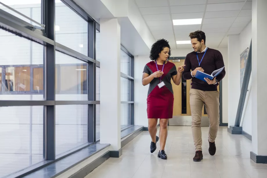 Two teachers are walking and talking together down the school hall in discussion..