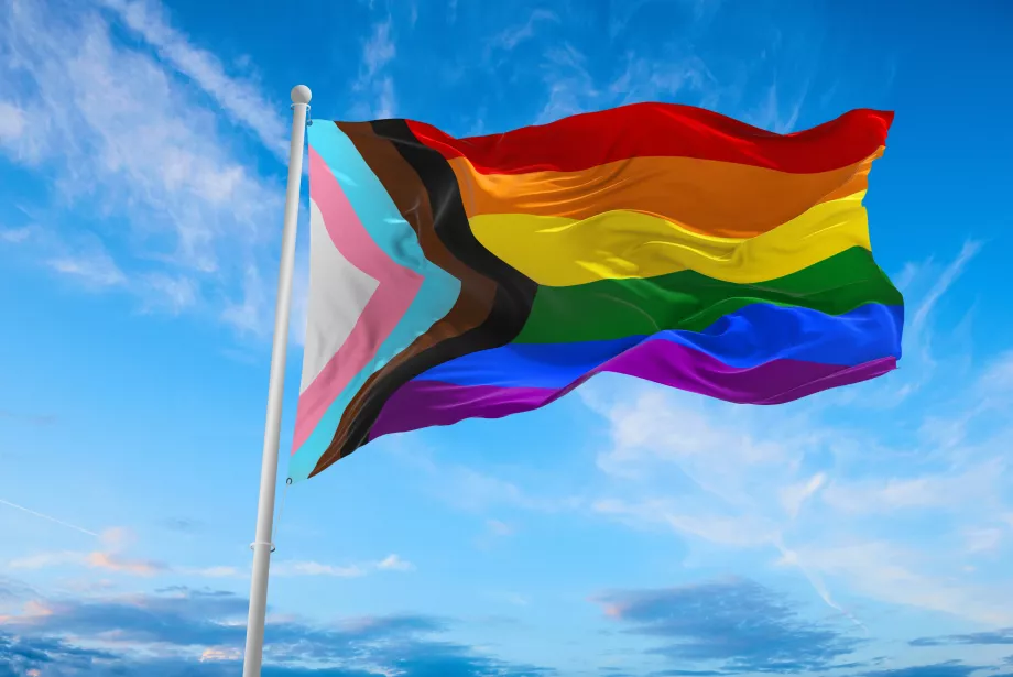 The Pride Progress flag flies against a blue sky.