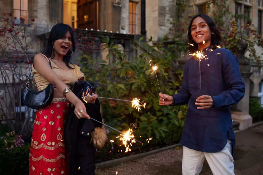 Two students hold sparklers outside the Trinity President's Lodgings.