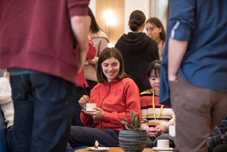 A student sits with a cup of team in a group.