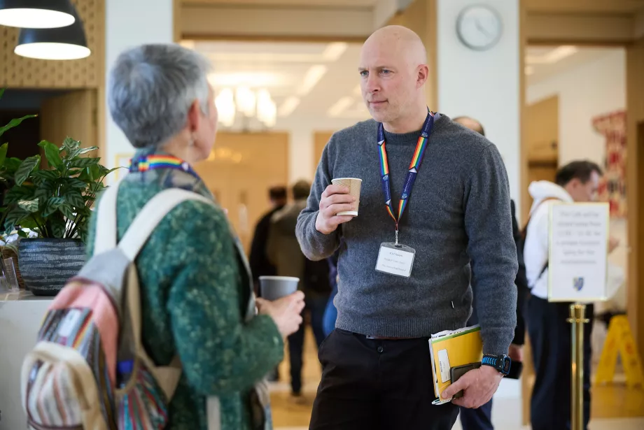 A male teacher stands with a cup of coffee talking to a female teacher in the Trinity College cafe.