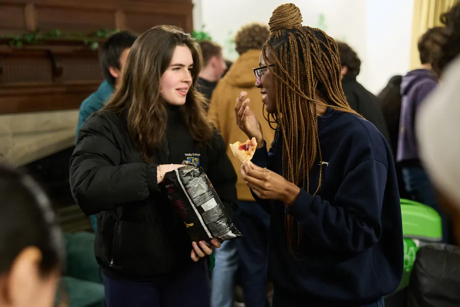 Two female students chat over snacks in the Trinity JCR. 
