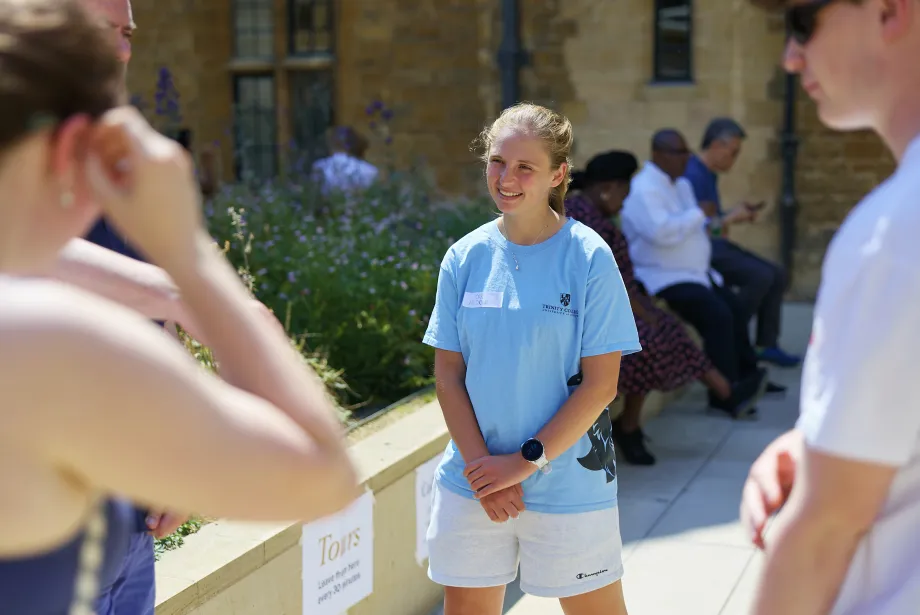 Trinity student ambassador Ore Jacobi stands in a blue t-shirt smiling and listening to prospective applicants during a college open day.